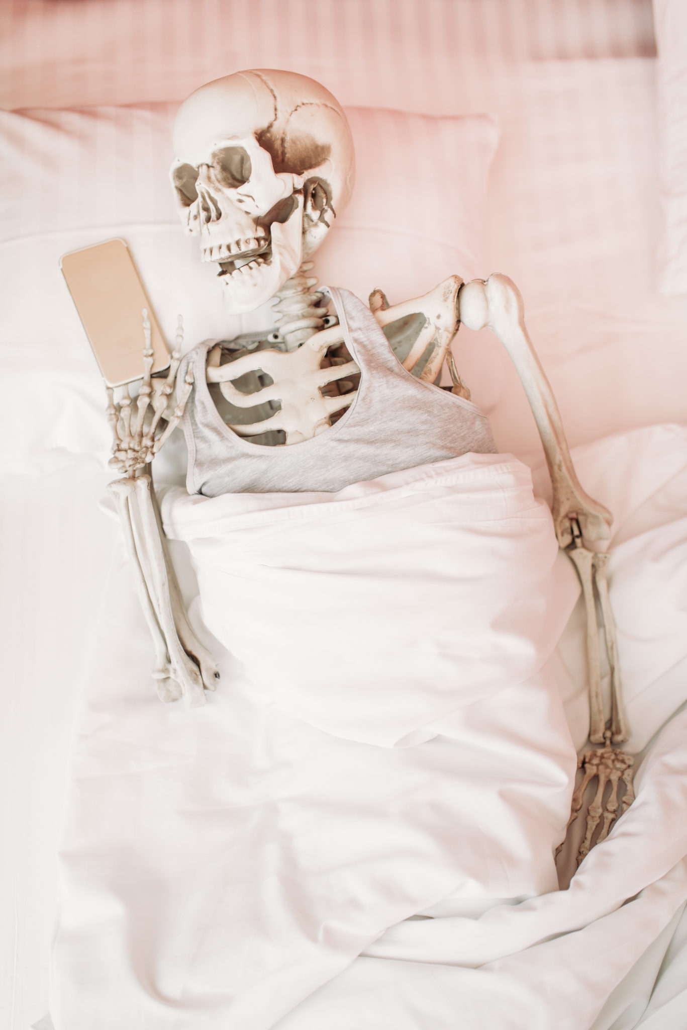 Human skeleton with phone in hand lies in bed social media for chiropractors